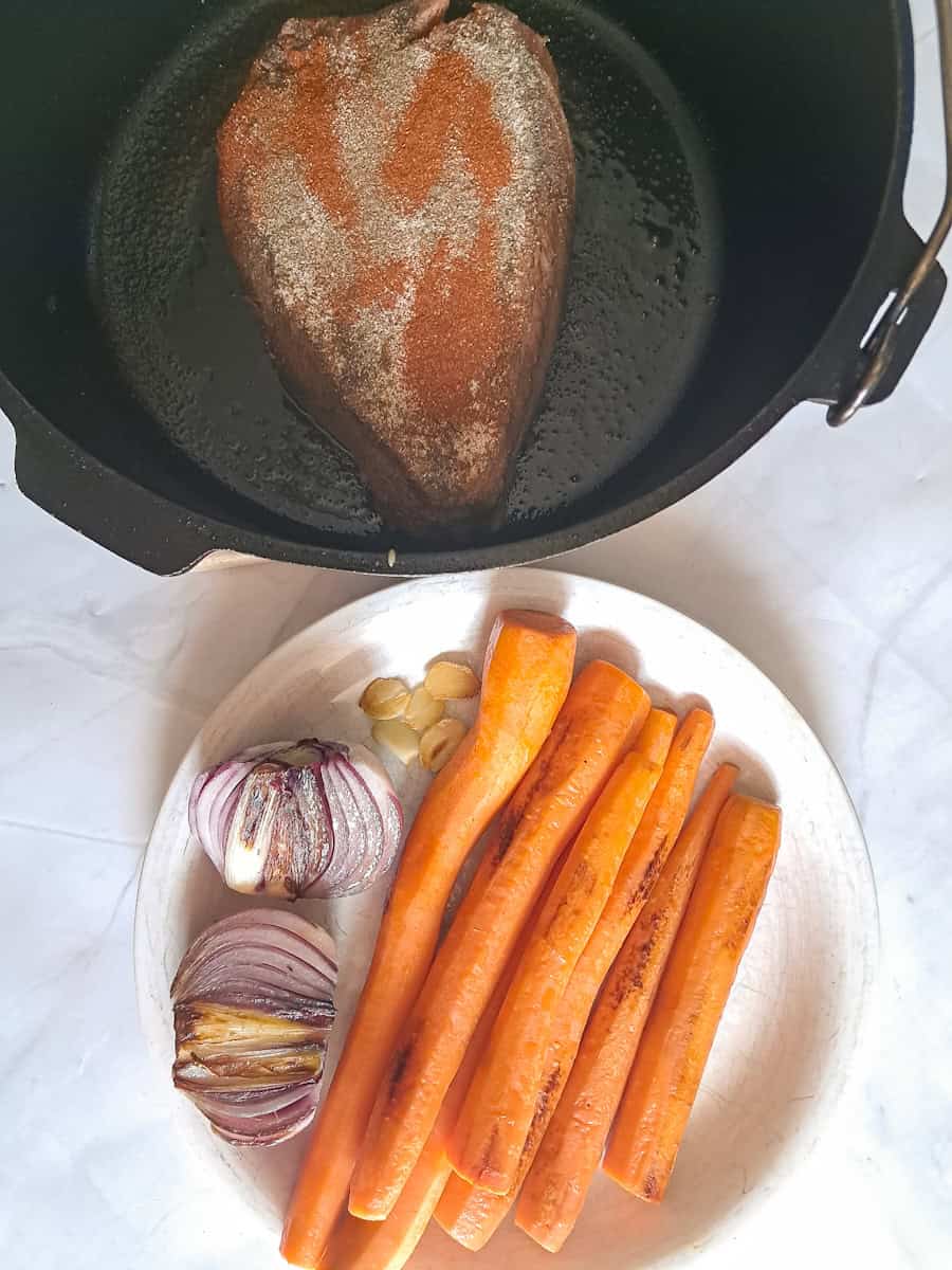 seasonings sprinkled over the roast and a plate of seared veggies ready to go back into the pot.