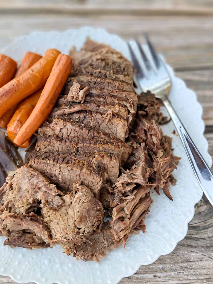 sliced roast beef on a large white plate with carrots and onions.