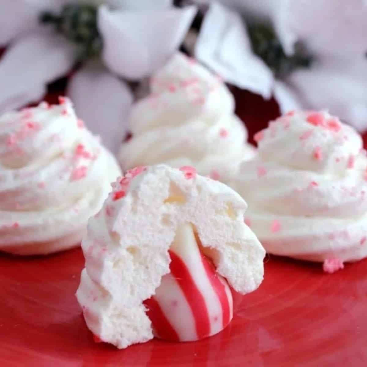 peppermint meringue cookies on a red plate, one is cut in half so you can see the peppermint kiss inside.