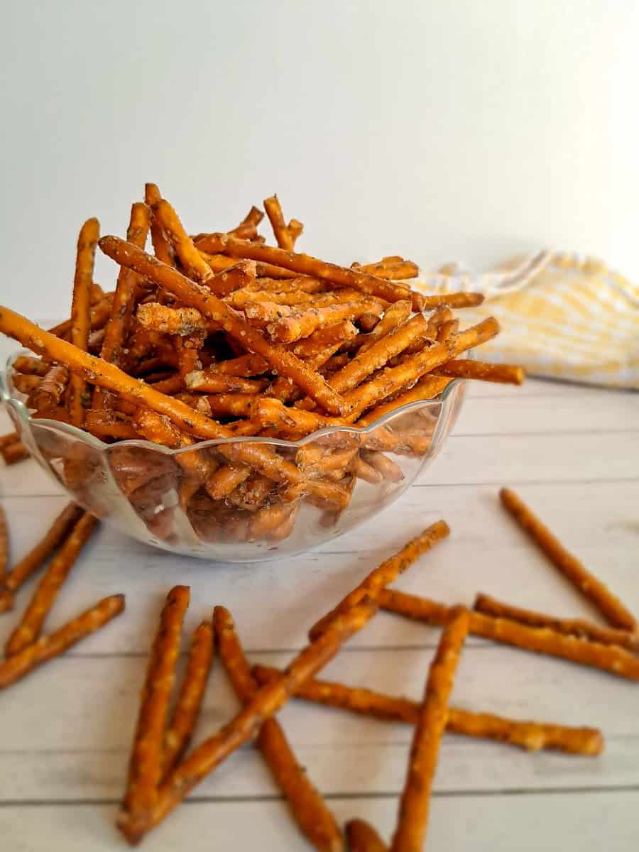 a glass bowl full of Amish seasoned pretzels and some scattered around.