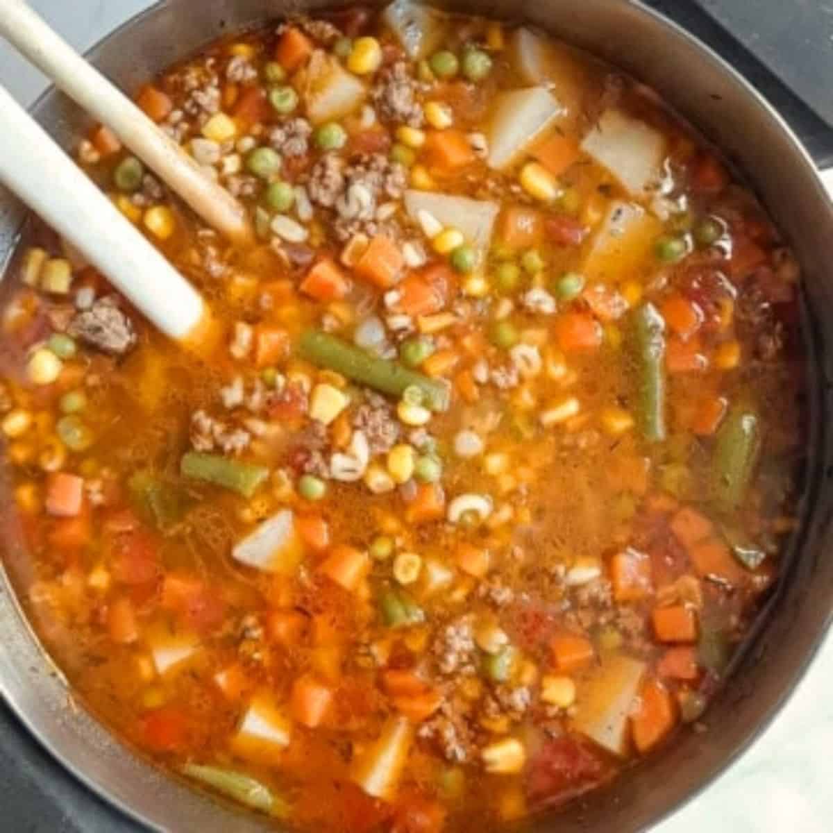 A large cooking pot full of vegetable soup soup with ground beef.