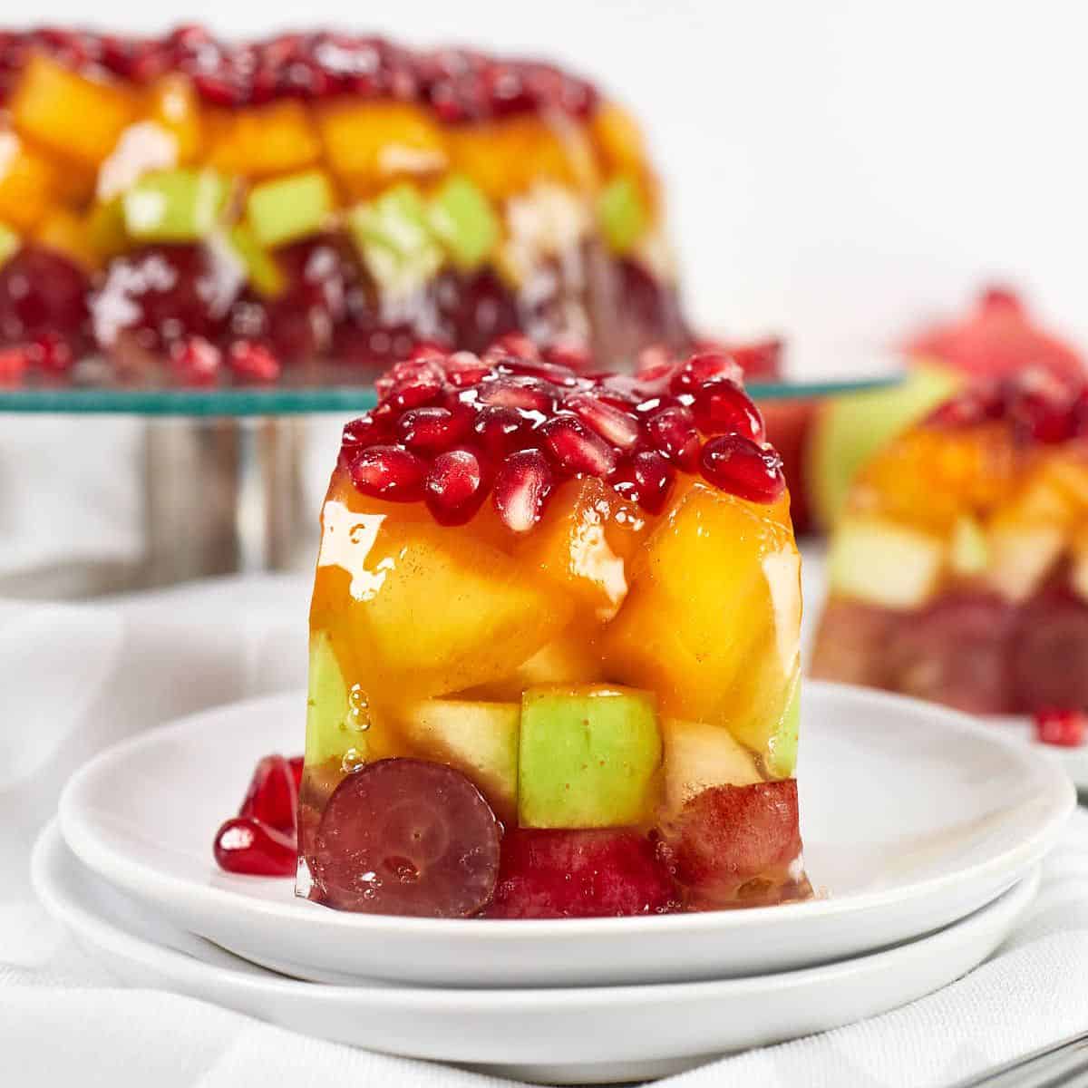 a slice of jello fruit cake on a plate with the remaining fruit cake in the background.