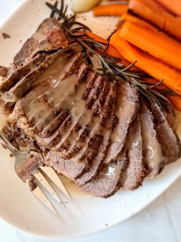 a plate of sliced roast beef with gravy on top and carrots on the side.