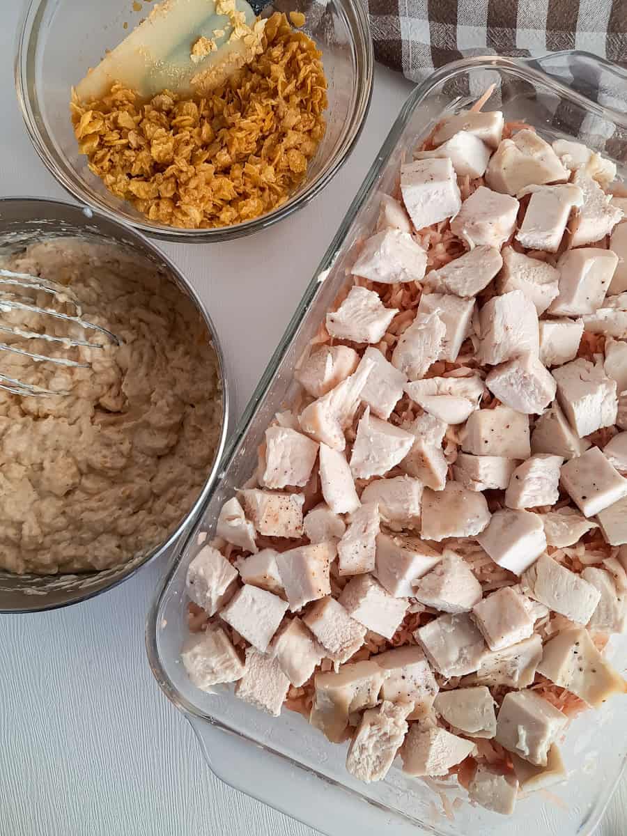 potatoes in a pan topped with cubed chicken breast, a pan with creamy sauce, and cornflake topping.