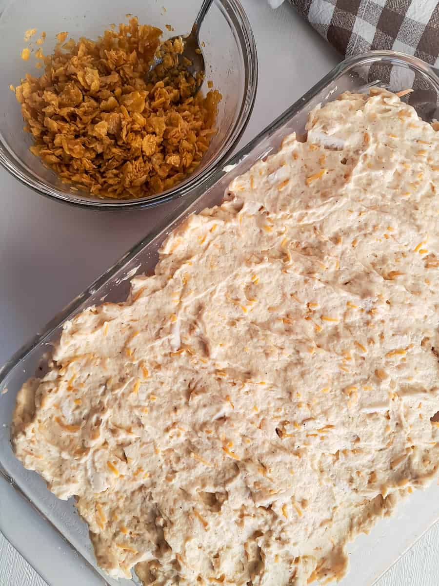 creamy sauce topped chicken and potatoes in a pan and cornflake topping in a bowl.