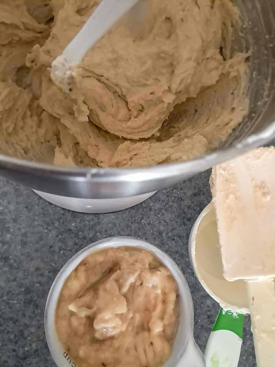 mixing banana batter in mixing bowl with a cup of mashed bananas on the side.