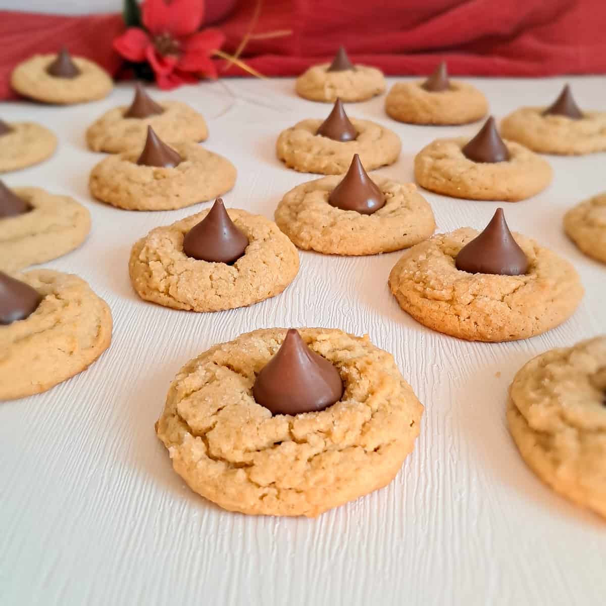 peanut butter blossom cookies topped with chocolate kisses scattered on a white background.