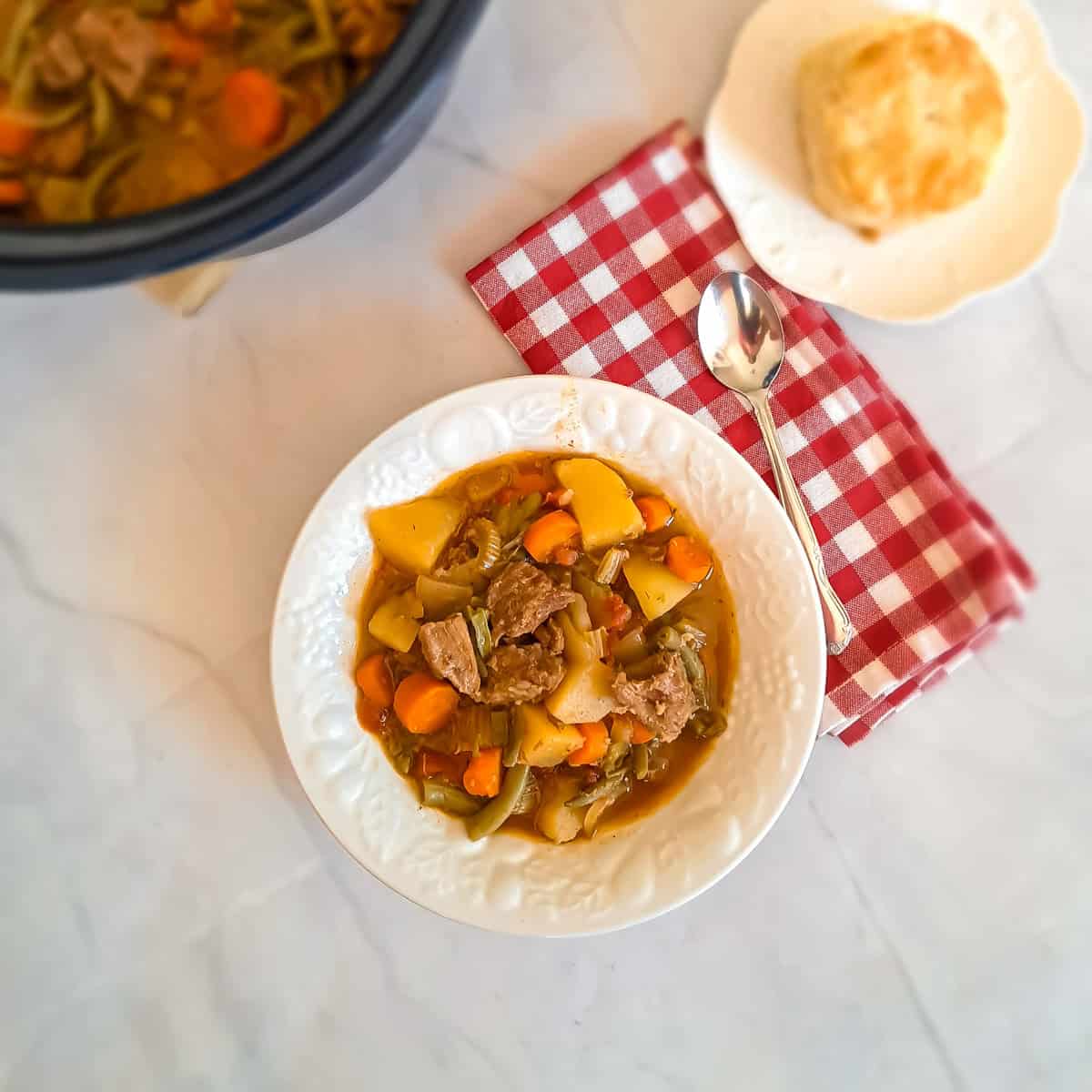 a bowl of Amish beef stew with a biscuit on a plate.
