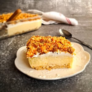 a slice of butterfinger dessert on a small plate with the remaining pan in the background.