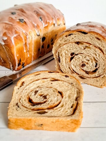 two loaves of Amish iced raisin swirl bread, one has a slice removed to reveal the beautiful cinnamon raisin swirls.