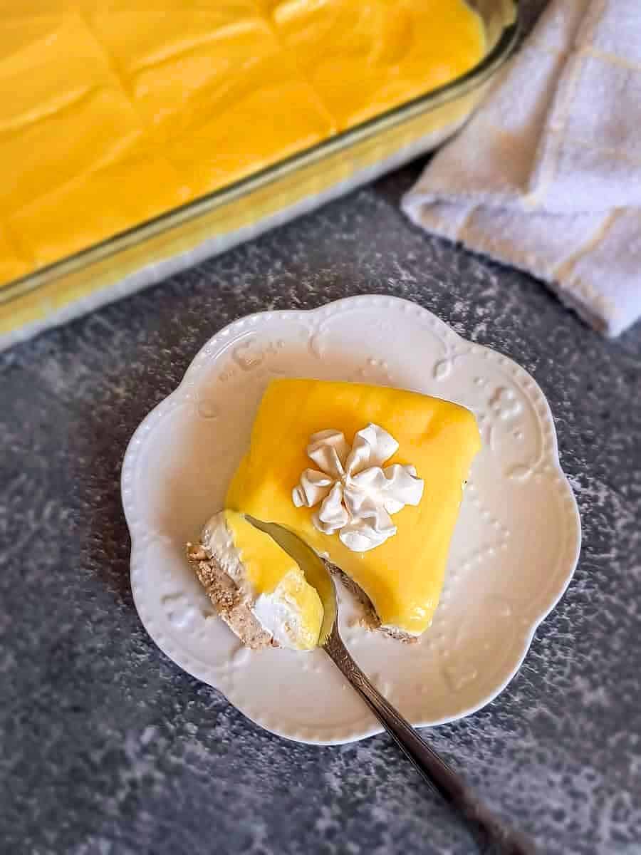 cutting into a slice of lemon lush dessert on a small plate.