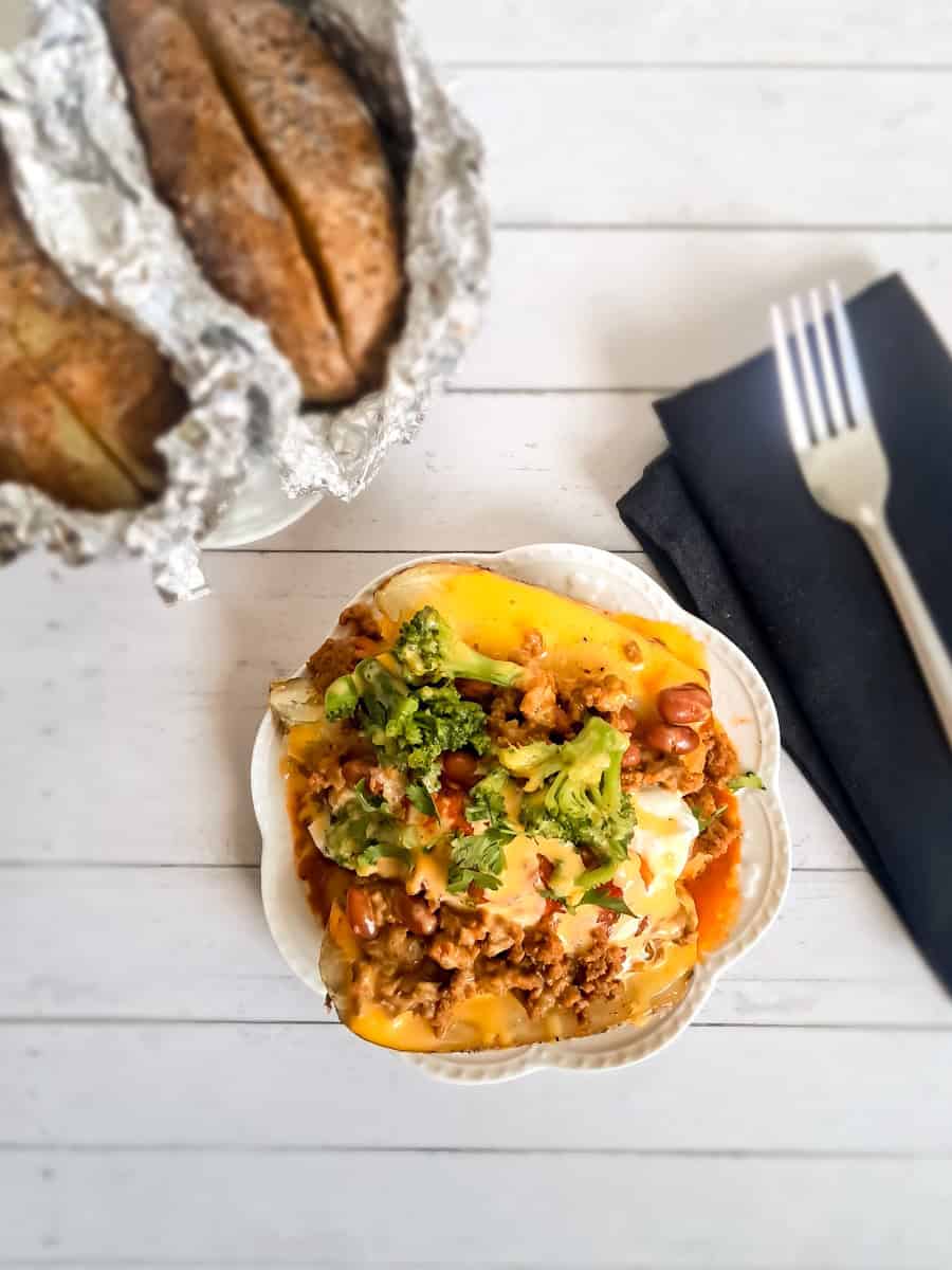 a baked potato on a plate with lots of toppings on and more baked potatoes in the background.