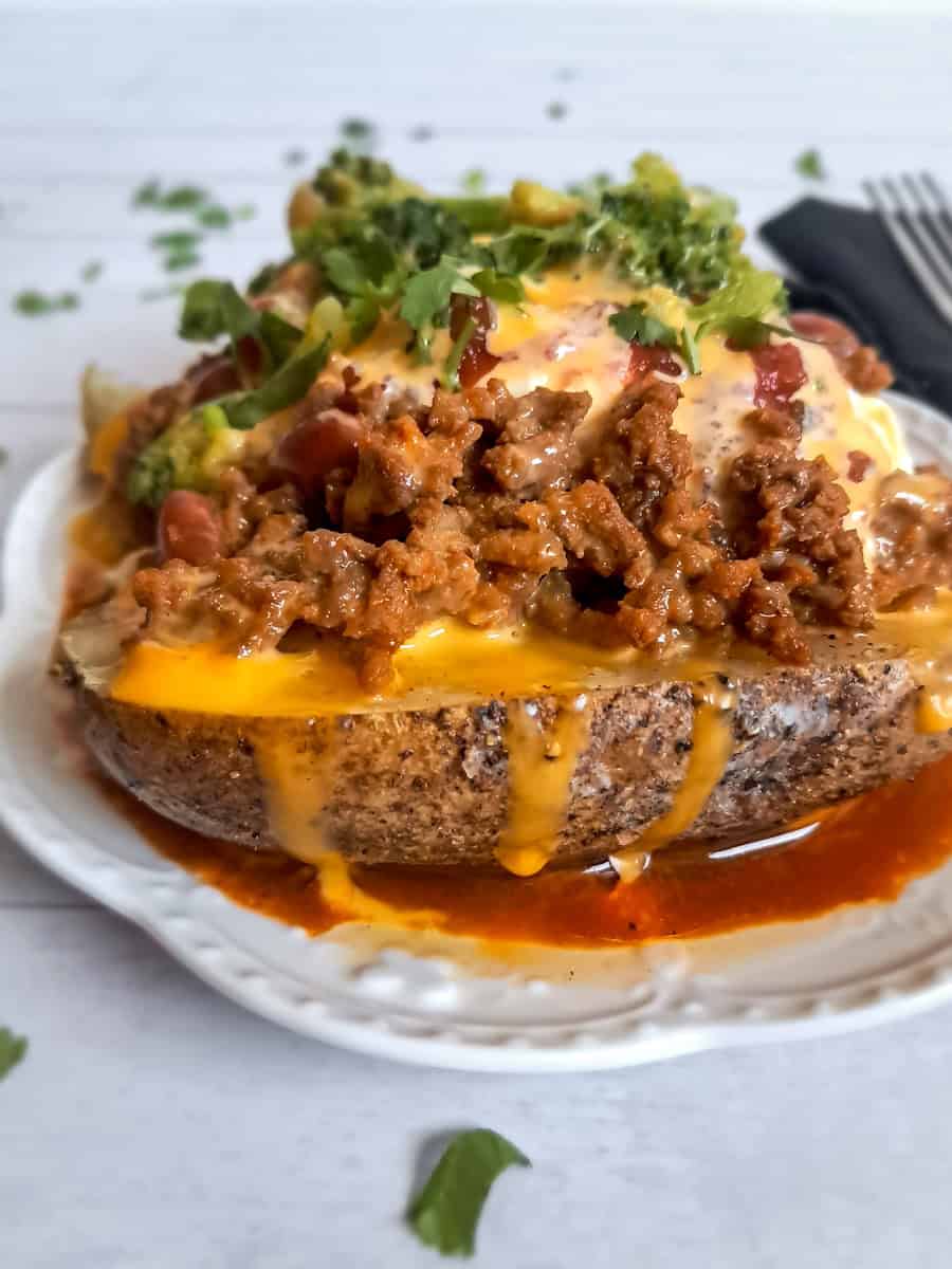 a baked potato piled with toppings: meat, beans, cheese sauce, sour cream, salsa, cilantro, and a bit of steamed broccoli.
