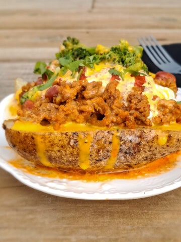 A large baked potato on a plate piled with toppings.