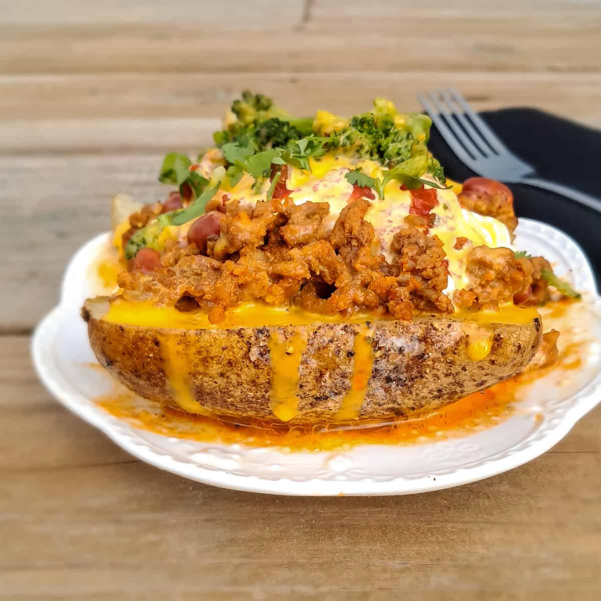 A large baked potato on a plate piled with toppings.