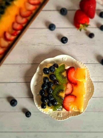a slice of homemade fruit pizza with sugar cookie crust, cream cheese filling, fruit, and glaze topping.