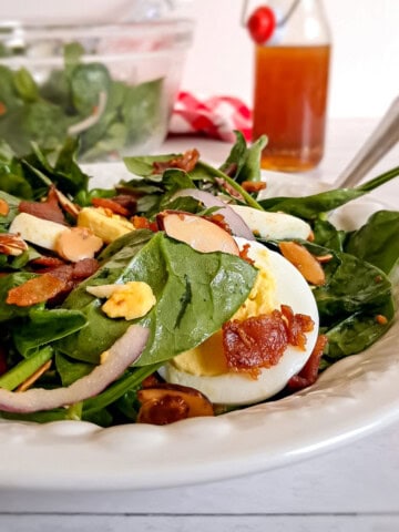 a bowl of spinach salad with eggs and bacon tossed with homemade vinegarette dressing.