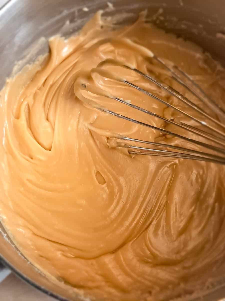a saucepan with a whisk in stovetop caramel icing.