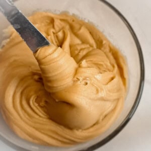 a bowl of homemade Amish caramel frosting with a knife in it to show the spreadable texture.