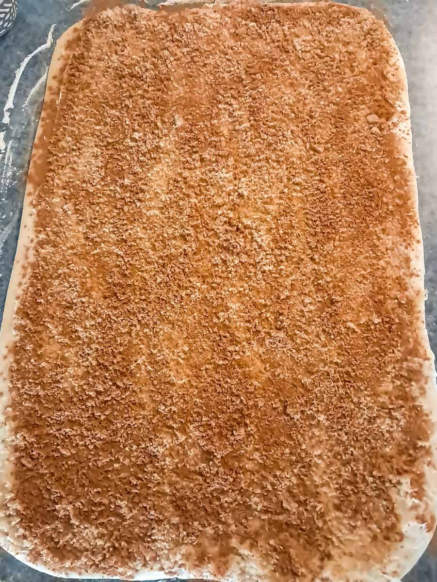 rolled out dough is covered in butter, brown sugar, and cinnamon.