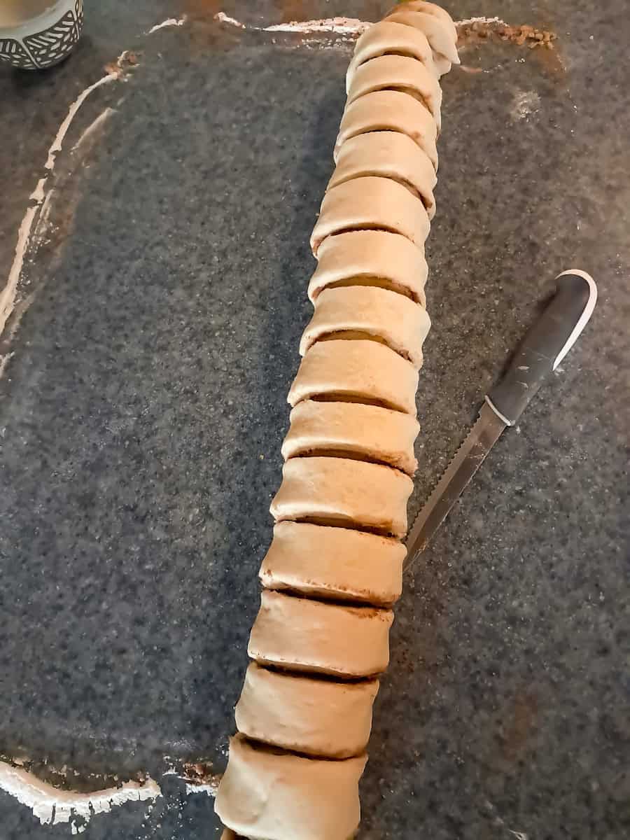 the cinnamon roll log cut into slices ready to place in baking pan.