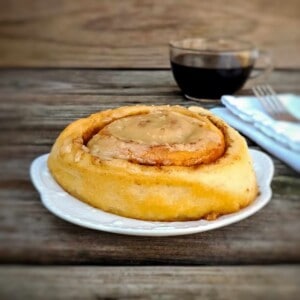 Amish cinnamon roll on a plate with a cup of coffee in background.