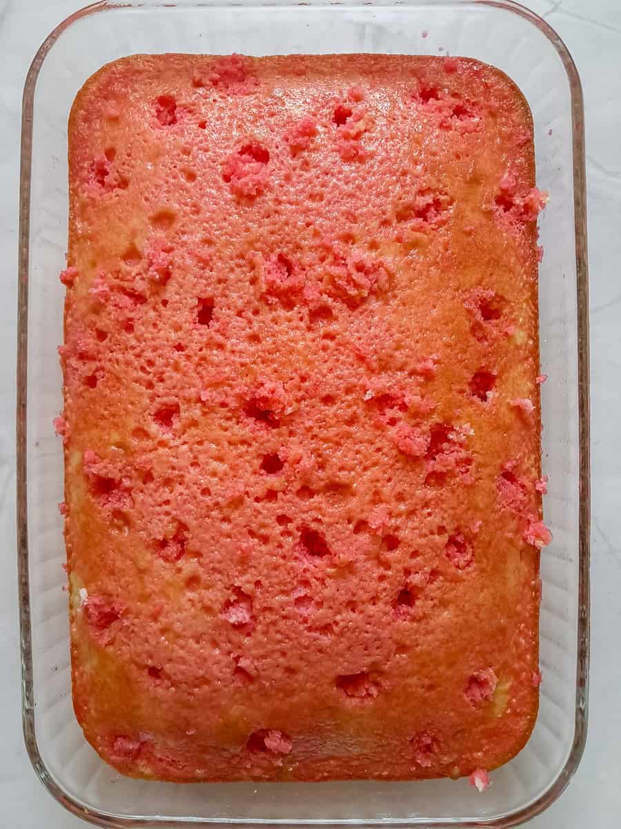 white cake in pan with holes poked and jello poured over the top.