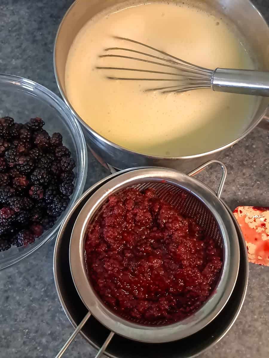 cooked custard in a saucepan, cooked berry sauce straining over a bowl, and extra berries in a bowl.