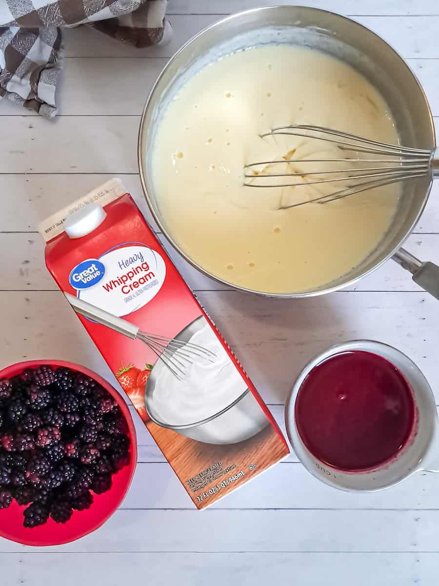 custard in sauepan, berry sauce in a cup, heavy cream, and berries: ready to mix the ice cream.