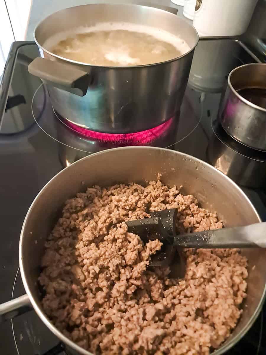 a pot with ground beef and another pot of macaroni cooking.