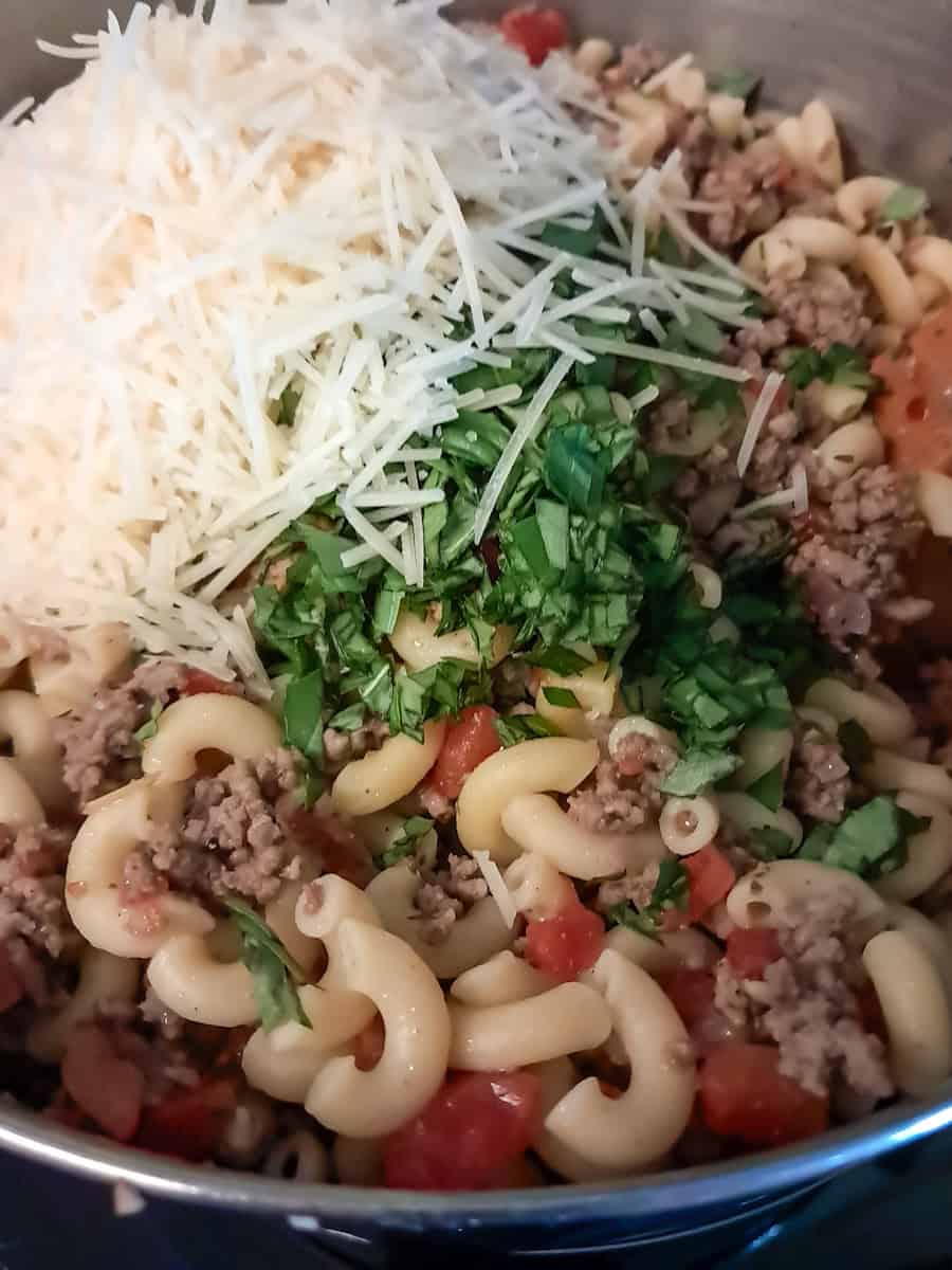 a pot of tomato and macaroni with parmesan cheese and fresh basil on top.
