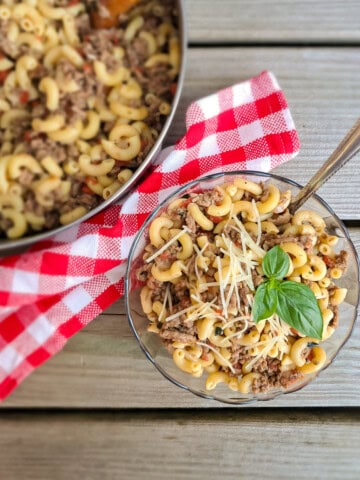 a bowl of macaroni and tomato with ground beef, and a large pot full sitting in the background.
