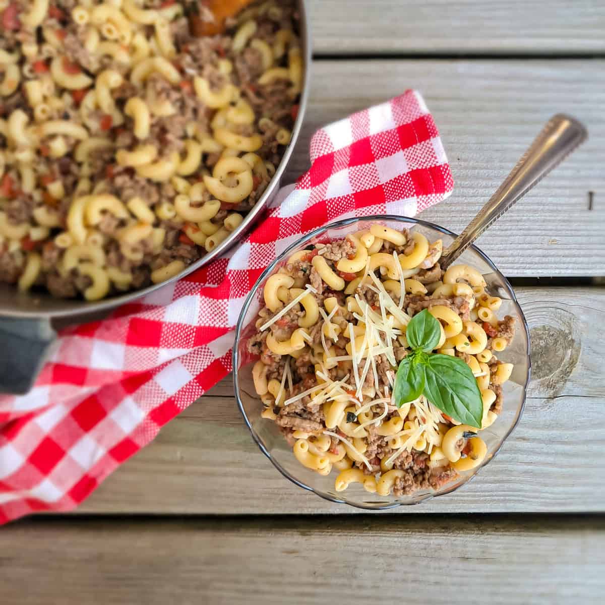 a bowl of macaroni and tomato with ground beef, and a large pot full sitting in the background.