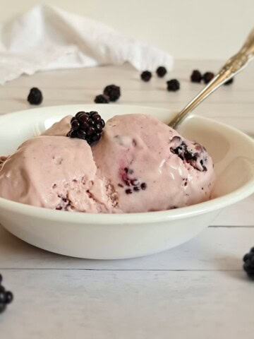 a small bowl with a couple scoops of homemade amish blackberry ice cream and blackberries scattered around.
