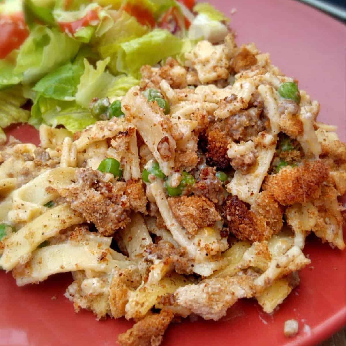 a red plate with yumasetti casserole and a side salad.