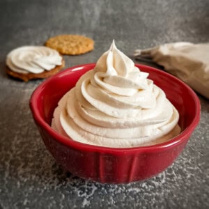 whoopie pie filling piped into a small red bowl, cookies in the background.