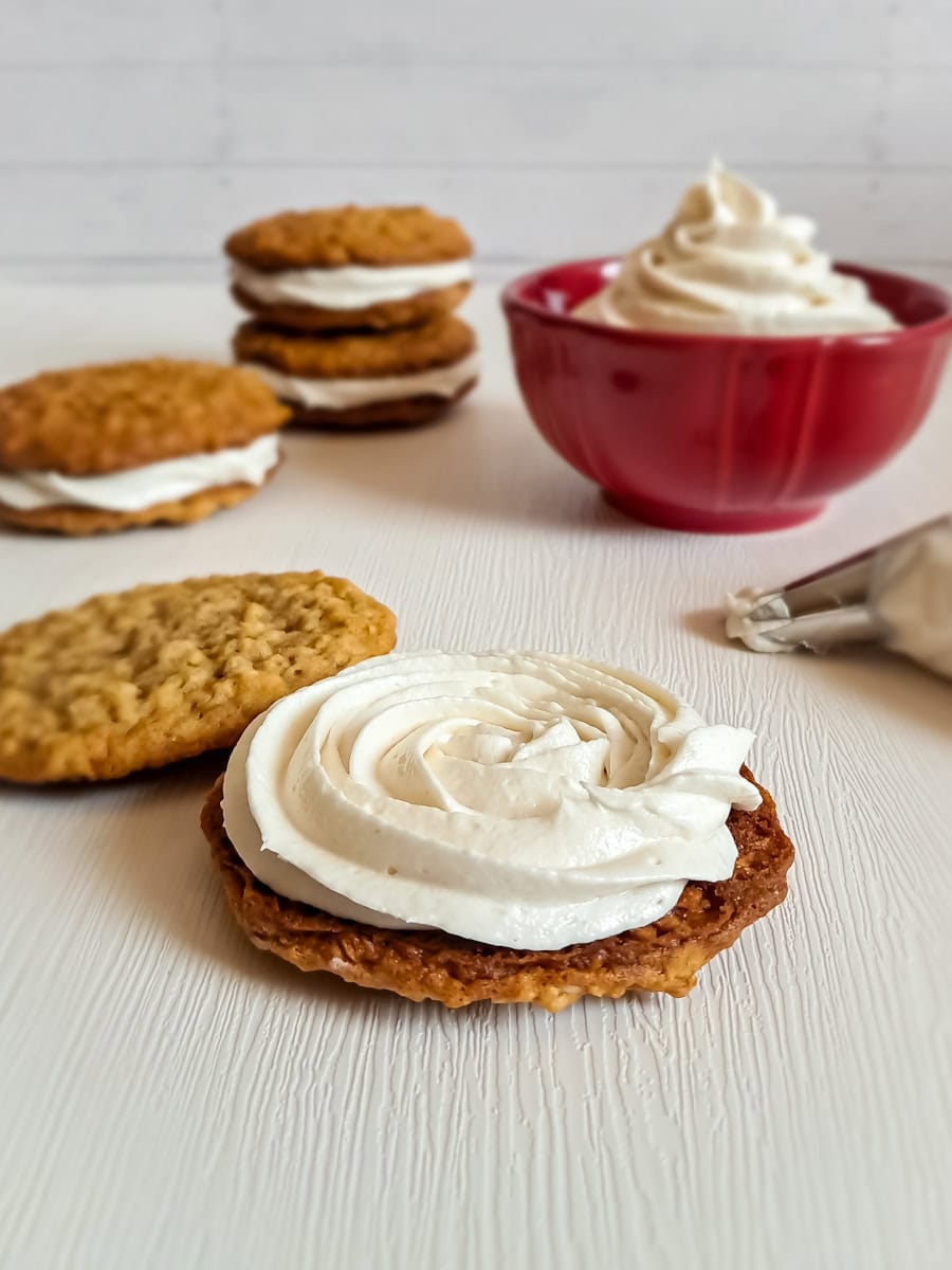 frosting piped onto an oatmeal cookie to make a whoopie pie and a bowl of filling and oatmeal whoopies in the background.