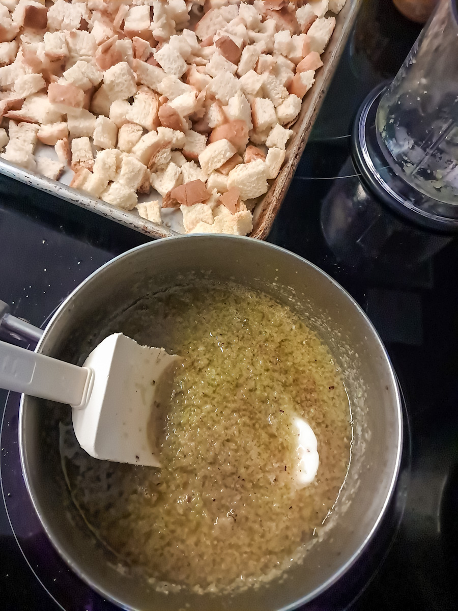 bread cubes on large tray, and butter/veggie mixture in saucepan on stove.