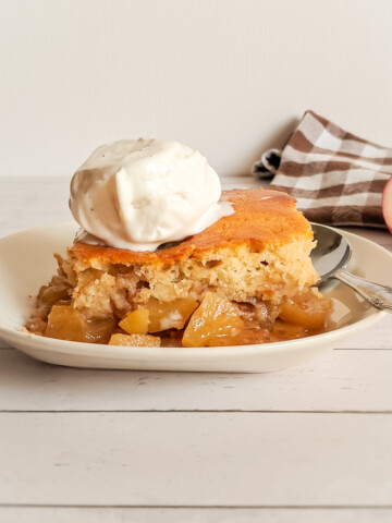 a slice of warm apple pudding cake on a small plate with a scoop of vanilla ice cream on top.