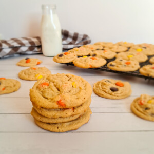 a stack of Amish peanut butter cookies with reese's pieces. more cookies and can of milk in the background.