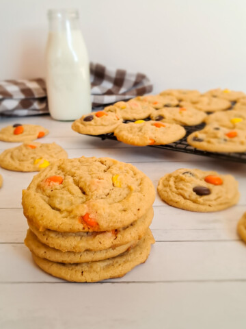 a stack of Amish peanut butter cookies with reese's pieces. more cookies and can of milk in the background.