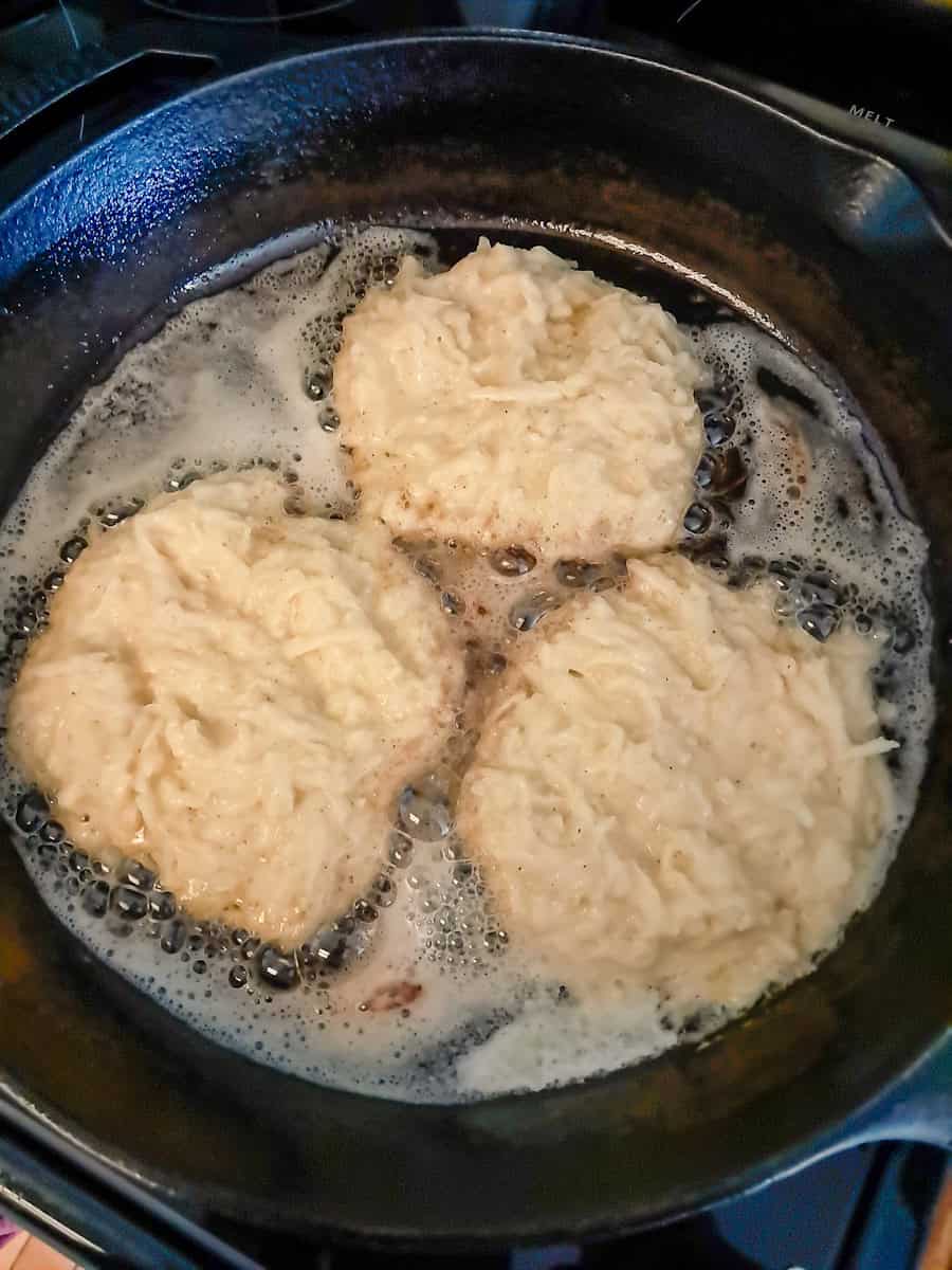 frying potato pancakes in butter and oil in a black cast iron skillet.