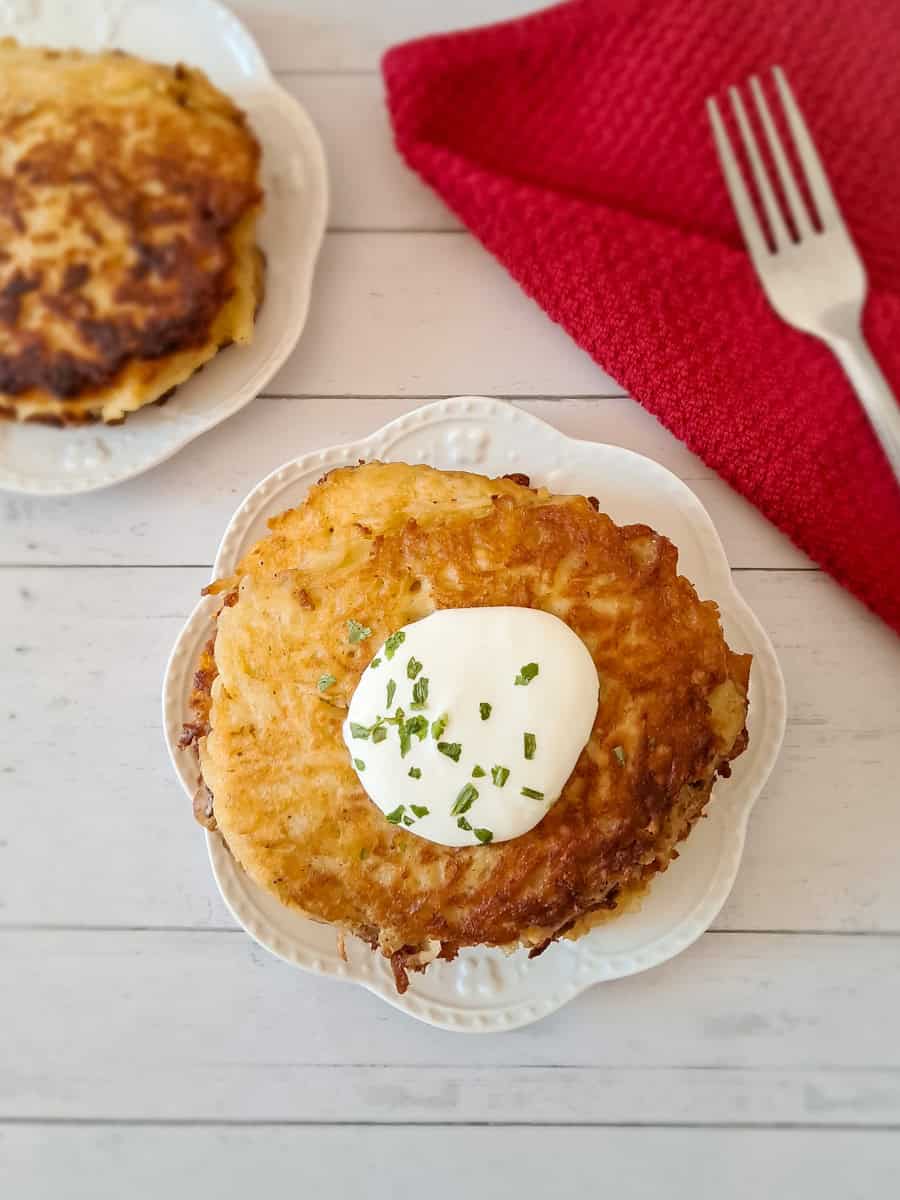2 plates with potato pancakes, one stack is topped with sour cream.