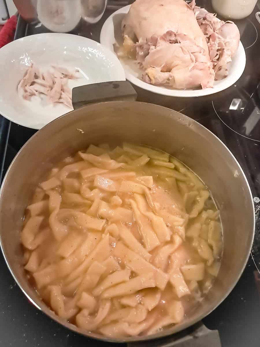noodles cooking in a large pot and a whole cooked chicken on a plate.