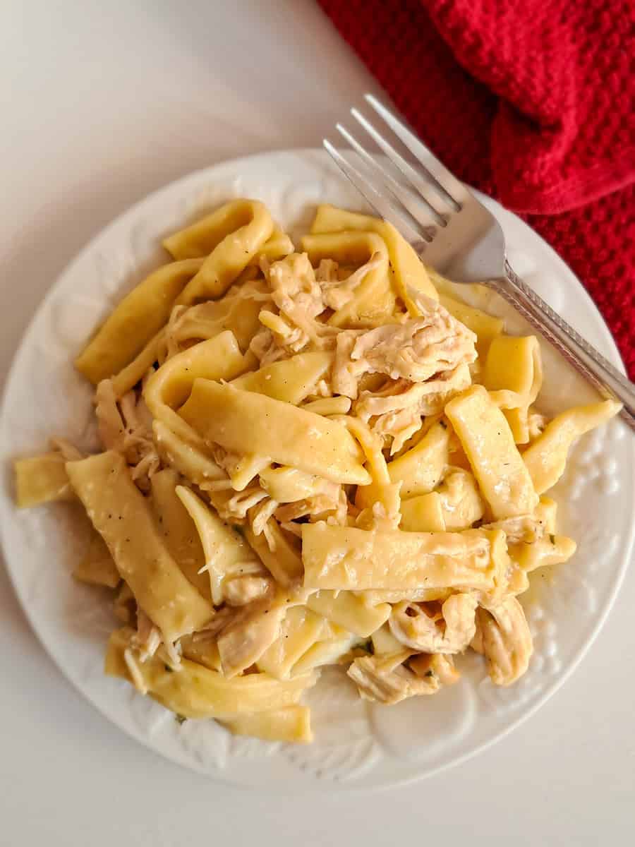 a plate piled full with mashed potatoes topped with homemade noodles and chicken.