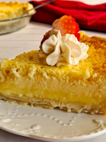 featuring a slice of Amish buttermilk pie with whipped cream and a strawberry slice on top.