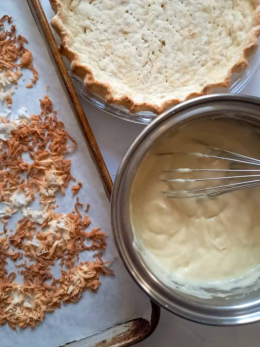 toasted coconut on a sheet pan, a prebaked pie crust, and the cooked custard filling in a large saucepan.