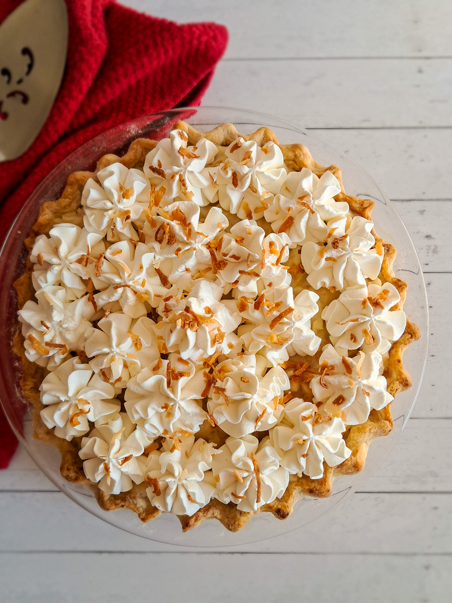 a whole 9" coconut pie topped with whipped cream and toasted coconut flakes.