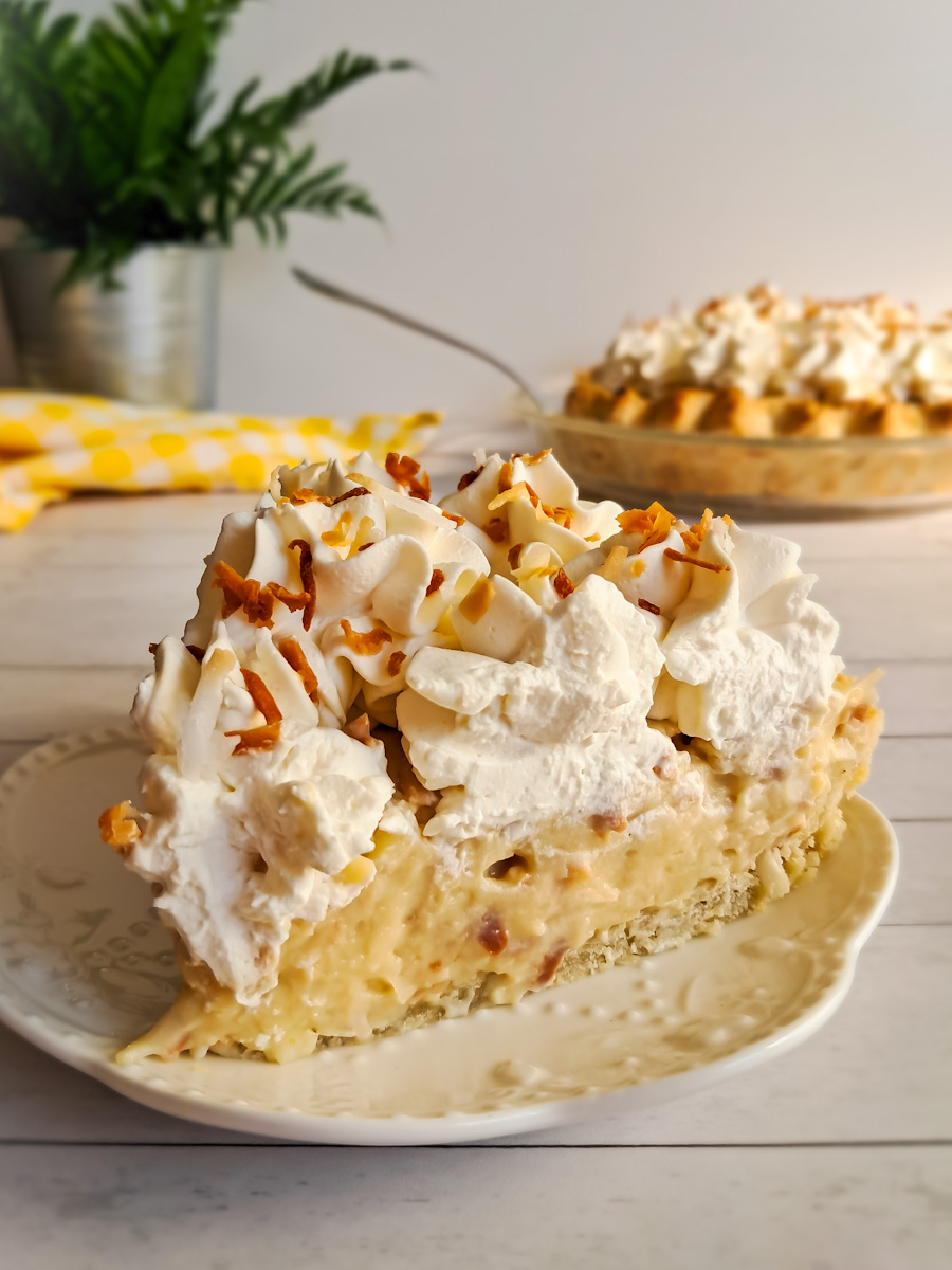 a slice of Amish coconut pie on a small plate and the remaining pie in the background.