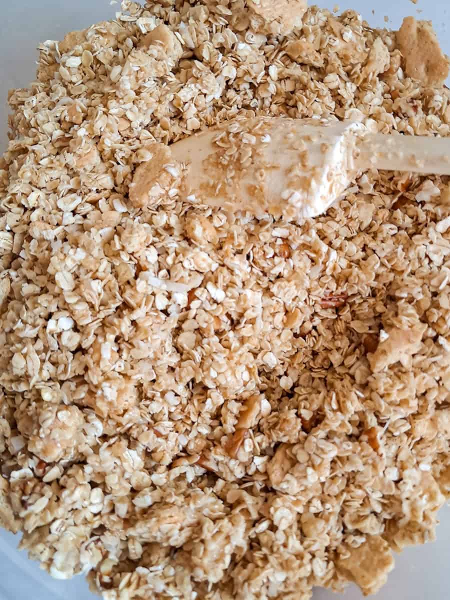 mixing homemade granola with oats, grahams, coconut, and pecans in a large bowl.